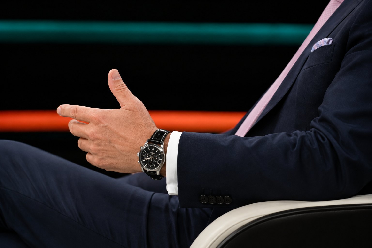 Mann im dunkelblauen Anzug mit einem Edelstahl-Chronographen am Handgelenk in einem Fernsehstudio